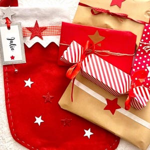 May include: A Christmas stocking and wrapped presents in festive colours. The red stocking has white stars and a tag with the name "Julie". Gifts are wrapped in red, brown, and white paper, decorated with red star accents and ribbons. A joyful holiday theme.