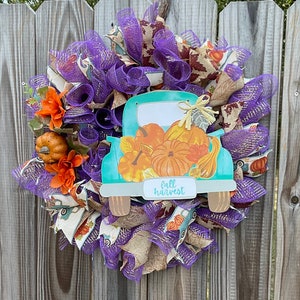 May include: A teal blue truck with a white cab and a bed full of pumpkins. The truck has a sign that says "fall harvest". The truck is surrounded by purple and brown mesh and orange flowers.