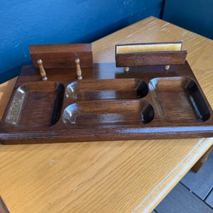 May include: A dark brown wooden desk organizer featuring a rectangular base with four recessed compartments. The unit includes two upright wooden back panels, one with two small decorative spindles, and a separate slot for holding papers.