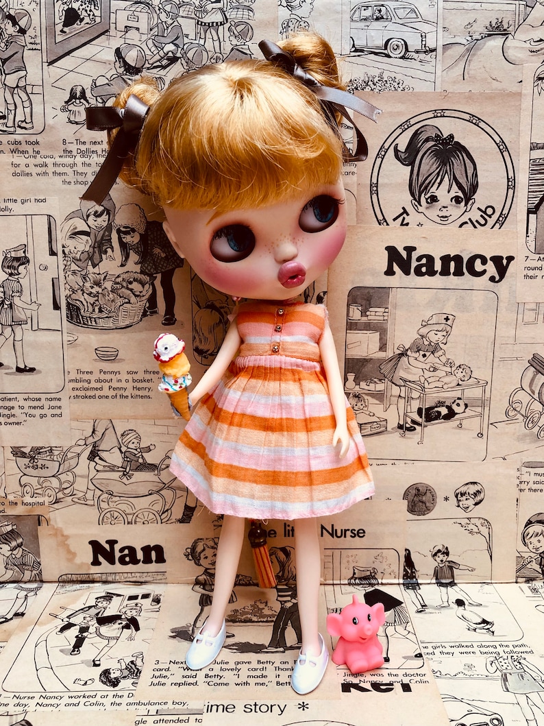 May include: A doll wearing a striped orange and pink dress and white shoes. The doll is holding a pink and white ice cream cone. The doll is standing in front of a background of vintage illustrations and text. The text includes the words "Nancy", "Nan", and "Nurse".