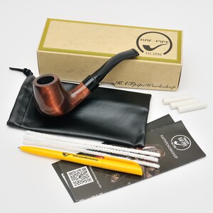 May include: A brown tobacco pipe with a black stem, presented with a black pouch, cleaning tools, and a yellow pen. The pipe is in front of a box with the text "KAF-PIPE Est.1996".