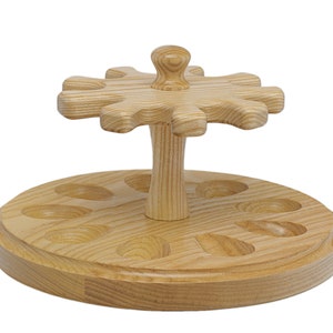 May include: A wooden pipe rack with a rotating top and eight slots for pipes. The rack is made of light wood and has a natural finish.