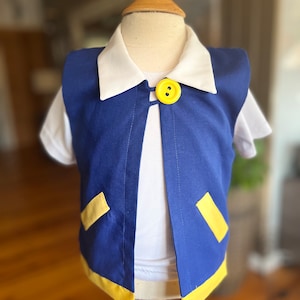 May include: A blue vest with yellow trim and a yellow button. The vest has a white collar and is worn over a white shirt.
