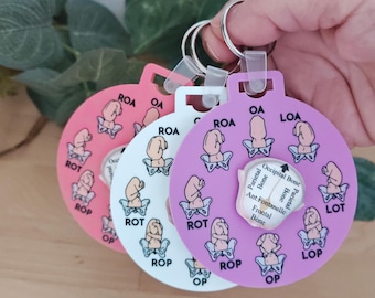 May include: Three circular keychains in pink, white, and purple, each featuring a rotating center disc. The discs display illustrations of fetal positions within a pelvis, labeled with abbreviations like OA, ROA, ROT, and ROP, plus anatomical text.