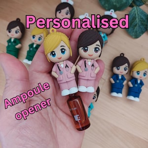May include: A set of personalized nurse figurines with a small glass bottle. The figurines are wearing pink scrubs and have a stethoscope around their necks. The text "Personalised" is written in pink letters above the figurines. The text "Ampoule opener" is written in pink letters below the figurines.