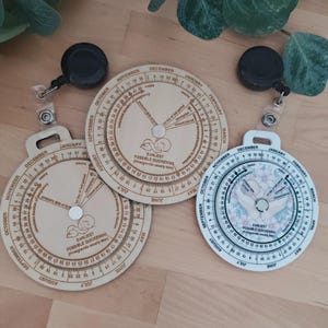 May include: Three circular pregnancy wheels with months and dates marked around the edges. The wheels are made of wood and white plastic. Each wheel has a rotating inner dial with pregnancy-related terms. The wheels are attached to retractable badge holders.