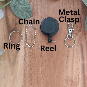 May include: A silver chain, ring, and retractable reel with a black plastic casing. A silver metal clasp is also included.