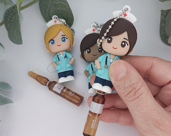 May include: Three nurse-themed keyrings with varying skin tones and hair colours. Each keyring features a miniature nurse figurine wearing a light blue uniform and a white cap. Two brown glass vials are also visible.