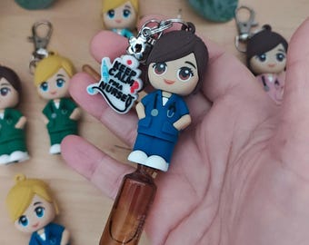 May include: A nurse-themed keyring featuring a miniature figurine in blue scrubs, a stethoscope, and brown hair. The keyring includes a charm with the text "Keep Calm I'm a Nurse." Other nurse figurines are visible in the background.