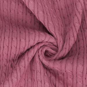 May include: Close-up of a soft, cable knit fabric in a rosy mauve color. The fabric is folded and draped, showcasing the texture and color.
