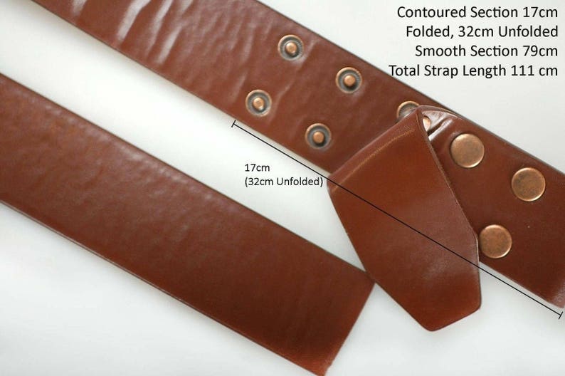 K&ouml;nnte beinhalten: Ein braunes Lederband mit einem konturierten Abschnitt, der 17 cm lang ist, wenn er gefaltet ist, und 32 cm lang, wenn er ausgeklappt ist. Das Band hat auch einen glatten Abschnitt, der 79 cm lang ist. Die Gesamtl&auml;nge des Bandes betr&auml;gt 111 cm.