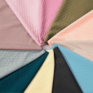 Peut inclure: Un assortiment d'&eacute;chantillons de tissus de diff&eacute;rentes couleurs et textures. Les &eacute;chantillons sont dispos&eacute;s en cercle, les bords de chaque &eacute;chantillon se chevauchant avec les bords des &eacute;chantillons adjacents. Tous les &eacute;chantillons sont matelass&eacute;s avec un motif en losange.