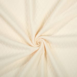 May include: Cream-colored fabric with a diamond pattern, arranged in a spiral. The fabric is soft and appears to be a knit or woven material. The texture is visible, with the diamond pattern adding visual interest to the textile.