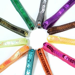 May include: A collection of colorful sequin trim ribbons in various shades, including green, silver, purple, brown, yellow, orange, turquoise, and pink. Each ribbon features a row of sequins sewn onto a fabric base, ideal for embellishments and crafts.