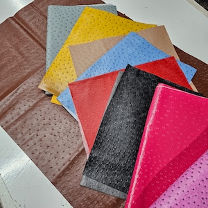 May include: A collection of ten different coloured faux leather sheets with an ostrich skin pattern. The sheets are arranged in a fan shape, with the brown sheet at the bottom and the pink sheet at the top.