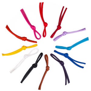 Può includere: Un assortimento di cordini in pelle di diversi colori, ognuno annodato con un nodo e un anello all'estremità. I cordini sono disposti in cerchio su uno sfondo bianco.