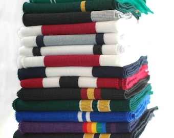 Puede incluir: Una pila de tela blanca, negra, roja, verde, azul y morada con rayas de colores. La tela está doblada y apilada en una pila.