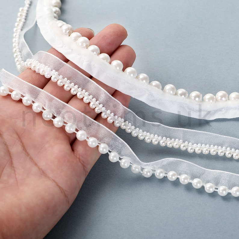 May include: Three white pearl trim ribbons with varying widths and pearl sizes. The ribbons are made of a sheer fabric and are perfect for adding a touch of elegance to any project.