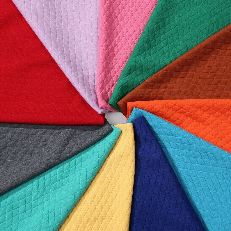 Peut inclure: Un assortiment de 12 &eacute;chantillons de tissus de diff&eacute;rentes couleurs et textures. Les &eacute;chantillons sont dispos&eacute;s en cercle, les bords se chevauchant. Les tissus sont tous matelass&eacute;s avec un motif en losange.