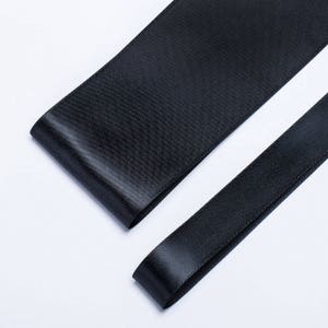 May include: Two black satin ribbons, one wider than the other, are laid out on a white surface.