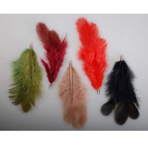 Puede incluir: Cinco plumas de diferentes colores con bucles de alambre unidos a la parte superior. Las plumas son verdes, rojas, marrones, negras y naranjas.