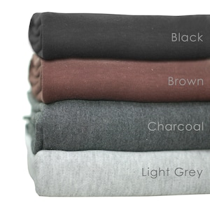 May include: A stack of four fabric swatches in different colors: black, brown, charcoal, and light grey. The swatches are folded and stacked on top of each other.
