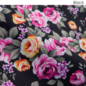 K&ouml;nnte beinhalten: Schwarzer Stoff mit einem floralen Muster mit rosa, gelben und wei&szlig;en Rosen. Der Stoff hat einen dezenten Glanz und eine weiche Textur.