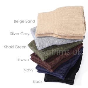 May include: A stack of knitted headbands in various colors, including beige sand, silver grey, khaki green, brown, navy, and black. The image displays the product's color options with the names of each color next to the corresponding headband.
