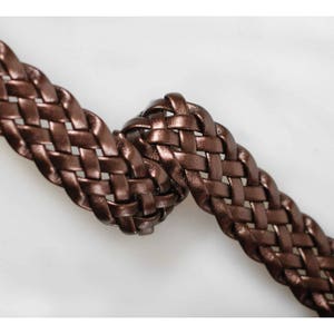 Peut inclure: Un gros plan sur une ceinture en cuir tress&eacute; marron. Le cuir est tiss&eacute; en un motif serr&eacute; et complexe.