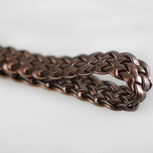 Peut inclure: Un gros plan sur une sangle tress&eacute;e en cuir marron. La sangle est tiss&eacute;e en un motif serr&eacute; et complexe.