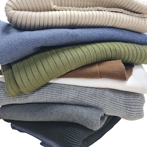 May include: A stack of six knitted jumpers in various colours, including beige, blue, green, brown, grey, and black.
