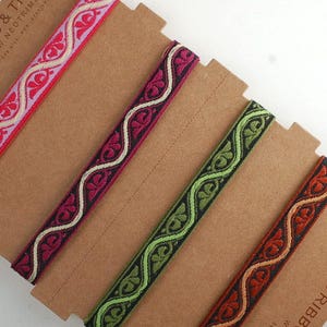 Può includere: Cinque diversi nastri decorativi con motivi diversi, mostrati su uno sfondo marrone. I nastri sono in tonalità di rosa, rosso, verde e arancione.