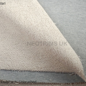 Puede incluir: Primer plano de una tela gris plata jaspeada con un bucle de felpa francesa, sin cepillar. La tela est&aacute; doblada para mostrar el interior y el exterior del material.