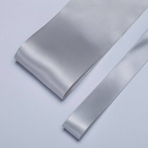 May include: Two rolls of silver satin ribbon. The ribbon is smooth and shiny.
