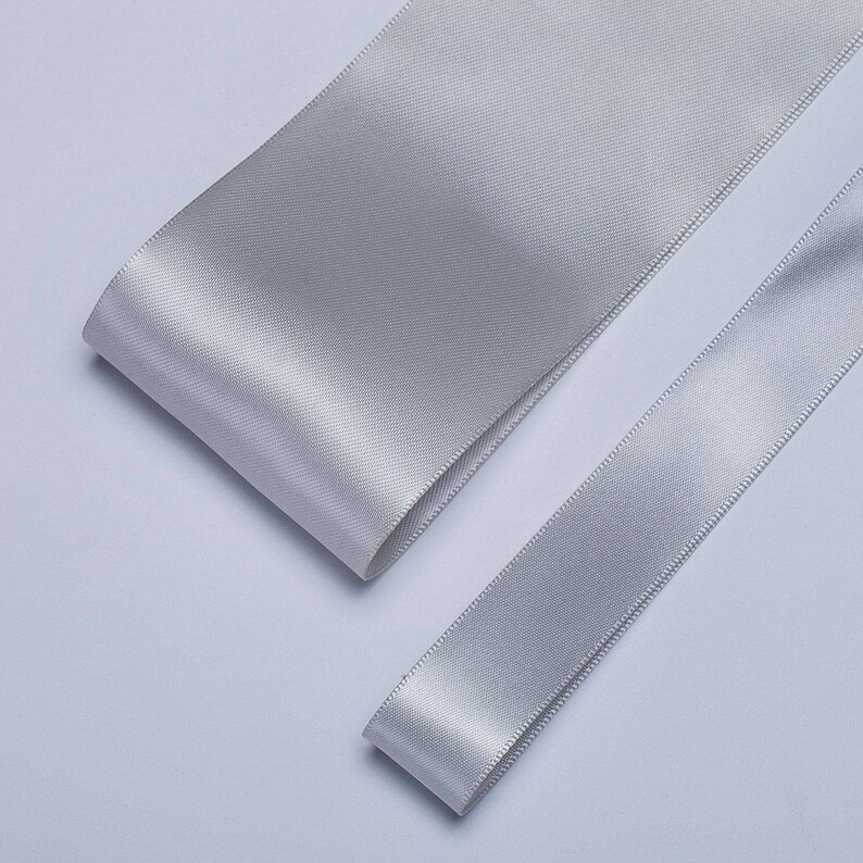 May include: Two rolls of silver satin ribbon. The ribbon is smooth and shiny.
