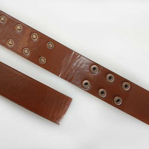 K&ouml;nnte beinhalten: Ein brauner Lederg&uuml;rtel mit Metall&ouml;sen. Der G&uuml;rtel ist in der Mitte durchgeschnitten, so dass man die Innenseite des Leders sieht.