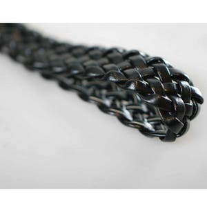 Peut inclure: Gros plan sur une sangle en cuir tress&eacute; noir. La sangle est tiss&eacute;e en un motif serr&eacute; et complexe.