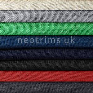 Könnte beinhalten: Ein Stapel Burlap-Stoff in verschiedenen Farben, darunter Beige, Weiß, Grau, Grün, Blau, Schwarz, Rot, Dunkelgrau und Braun. Der Stoff ist mit einer lockeren, offenen Webart gewebt.