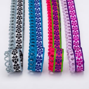 May include: Four different trims of ribbon with scalloped edges and a repeating pattern of small hearts. The trims are in shades of blue, pink, green, and purple.
