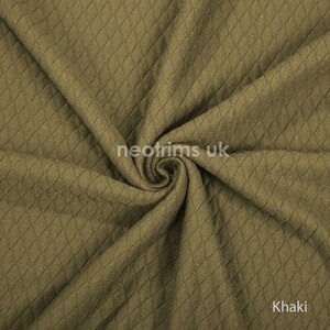 K&ouml;nnte beinhalten: Khakifarbener Stoff mit Rautenmuster. Der Stoff ist gefaltet und zeigt Textur und Tiefe. Das Wort "Khaki" ist in der unteren rechten Ecke sichtbar. Der Stoff scheint ein mittelschweres Material zu sein.