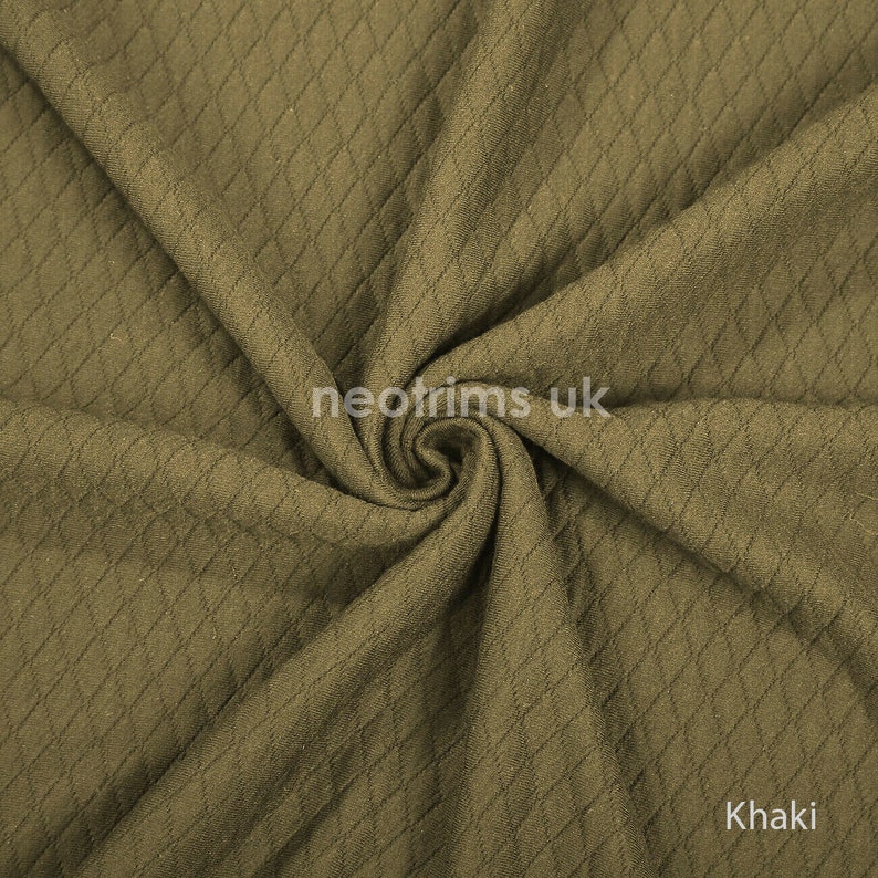 K&ouml;nnte beinhalten: Khakifarbener Stoff mit Rautenmuster. Der Stoff ist gefaltet und zeigt Textur und Tiefe. Das Wort "Khaki" ist in der unteren rechten Ecke sichtbar. Der Stoff scheint ein mittelschweres Material zu sein.