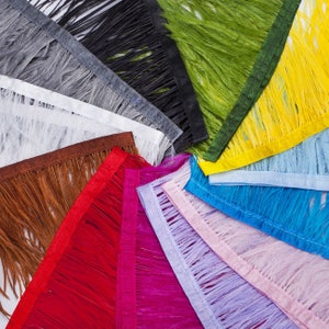 Op de afbeelding: Een verscheidenheid aan verenbies in verschillende kleuren, waaronder wit, bruin, rood, roze, paars, blauw, geel, groen, zwart en grijs. De veren zijn in een cirkelvormige opstelling gerangschikt, met de uiteinden van de veren naar buiten gericht.