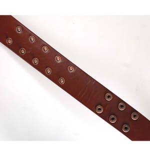K&ouml;nnte beinhalten: Ein brauner Lederg&uuml;rtel mit kupferfarbenen Nieten. Der G&uuml;rtel ist schr&auml;g dargestellt, wobei die Nieten oben und unten am G&uuml;rtel sichtbar sind.
