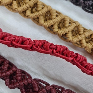 Puede incluir: Tres cordones de cuero trenzados en rojo, burdeos y marrón. Los cordones están entrelazados en un patrón complejo.
