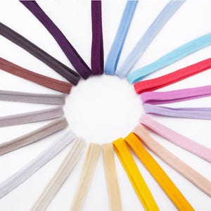 Puede incluir: Una variedad de colores de bandas el&aacute;sticas dispuestas en c&iacute;rculo sobre un fondo blanco. Los colores incluyen morado, marr&oacute;n, gris, blanco, beige, amarillo, naranja, rosa y rojo.