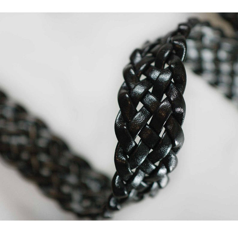 Peut inclure: Gros plan sur une sangle tress&eacute;e en cuir noir. La sangle est tiss&eacute;e en un motif serr&eacute; et complexe.