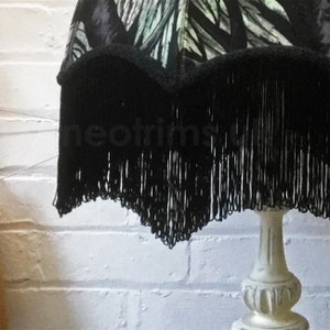 Puede incluir: Una pantalla de lámpara negra con un borde de flecos y un patrón floral blanco. La pantalla de la lámpara está sobre una base de lámpara blanca.