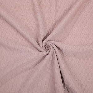 Peut inclure: Gros plan sur un tissu doux et rose avec un motif en losange textur&eacute;. Le tissu est pli&eacute; et drap&eacute;, cr&eacute;ant un aspect doux et fluide.