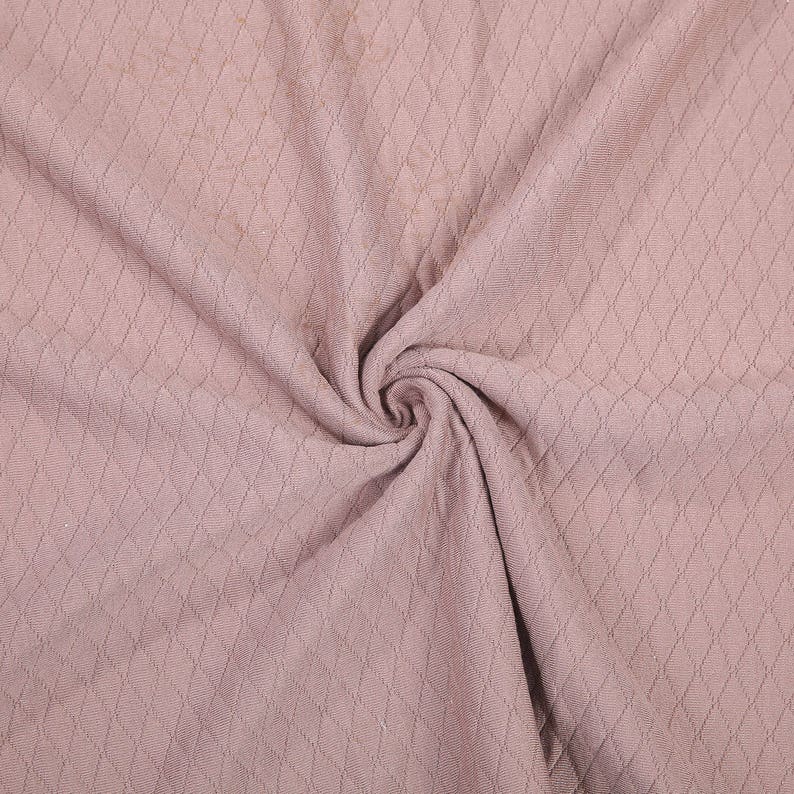 Peut inclure: Gros plan sur un tissu doux et rose avec un motif en losange textur&eacute;. Le tissu est pli&eacute; et drap&eacute;, cr&eacute;ant un aspect doux et fluide.
