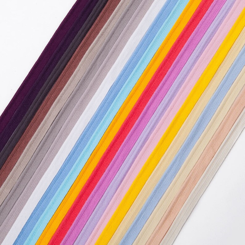 Puede incluir: Una colecci&oacute;n de gomas el&aacute;sticas para el cabello de colores en varios tonos de azul, rosa, amarillo, naranja y rojo. Las gomas el&aacute;sticas para el cabello est&aacute;n dispuestas en diagonal sobre un fondo blanco.
